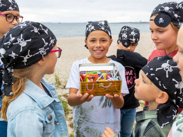 Kinder am Strand, die als Piraten verkleidet sind und eine Schatzkiste mit buntem Inhalt gefunden haben