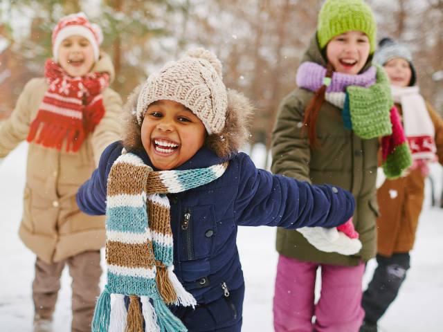 vier Kinder in Schneeanzügen laufen lachend durch den Schnee