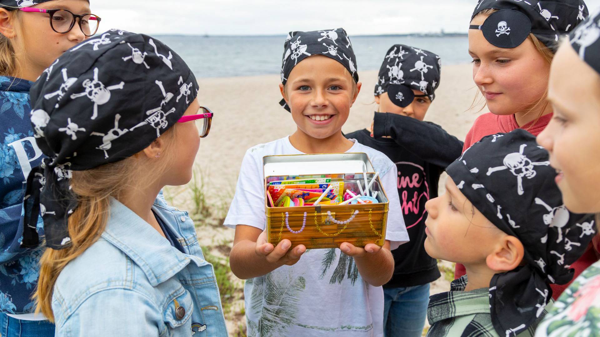 Kinder am Strand, die als Piraten verkleidet sind und eine Schatzkiste mit buntem Inhalt gefunden haben